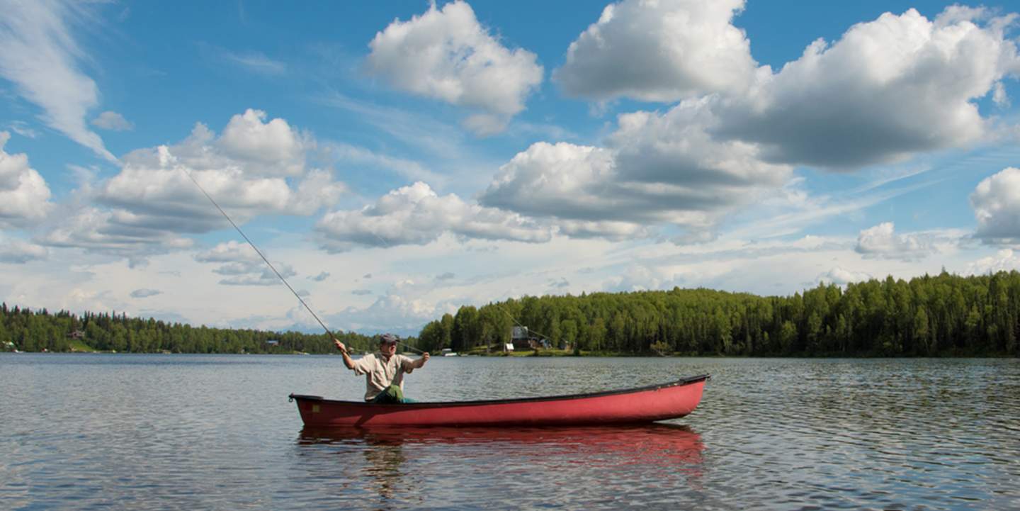 Man in a red boat fishing on a lake