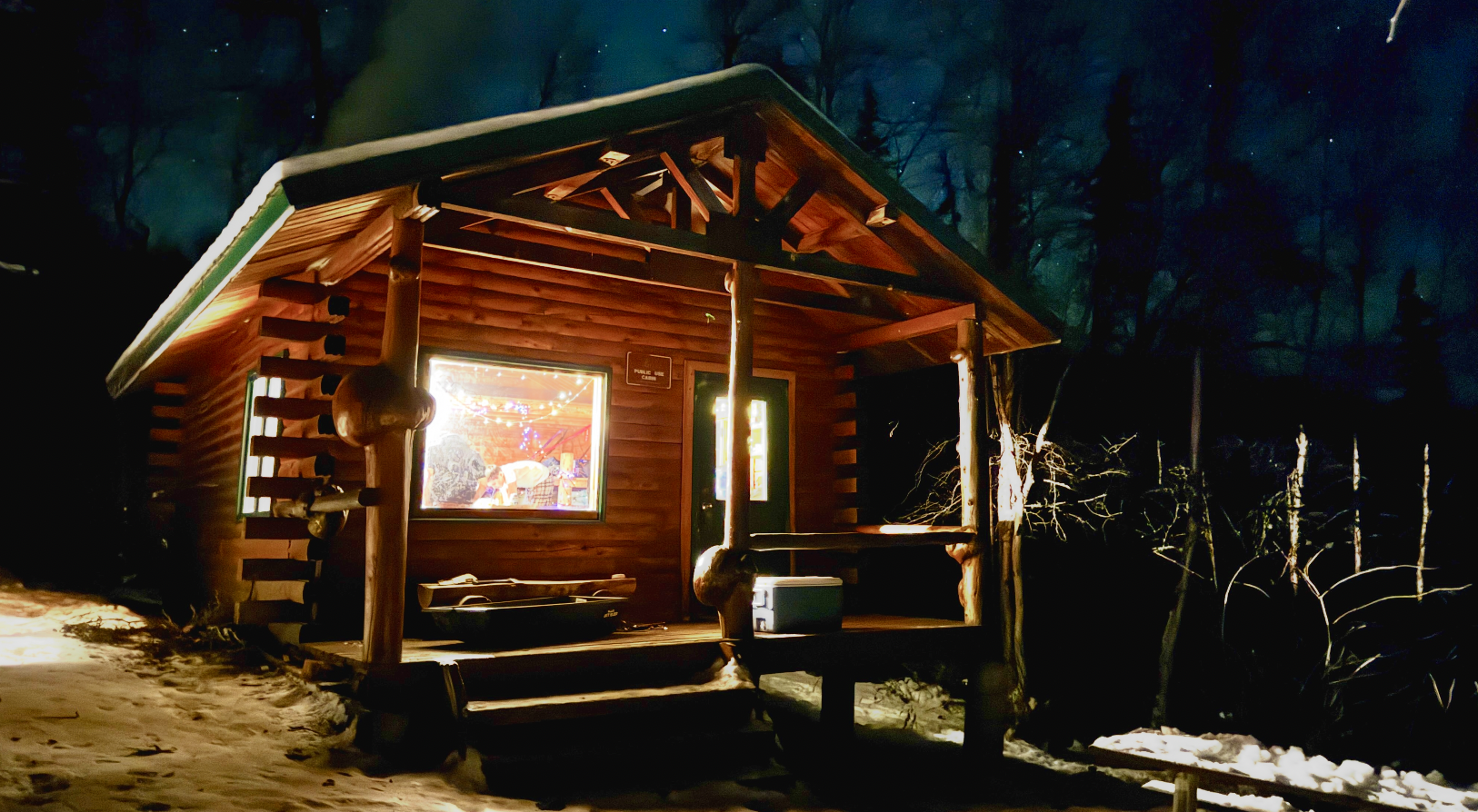 A cozy log cabin illuminated at night in a snowy forest setting in Mat-Su, Alaska
