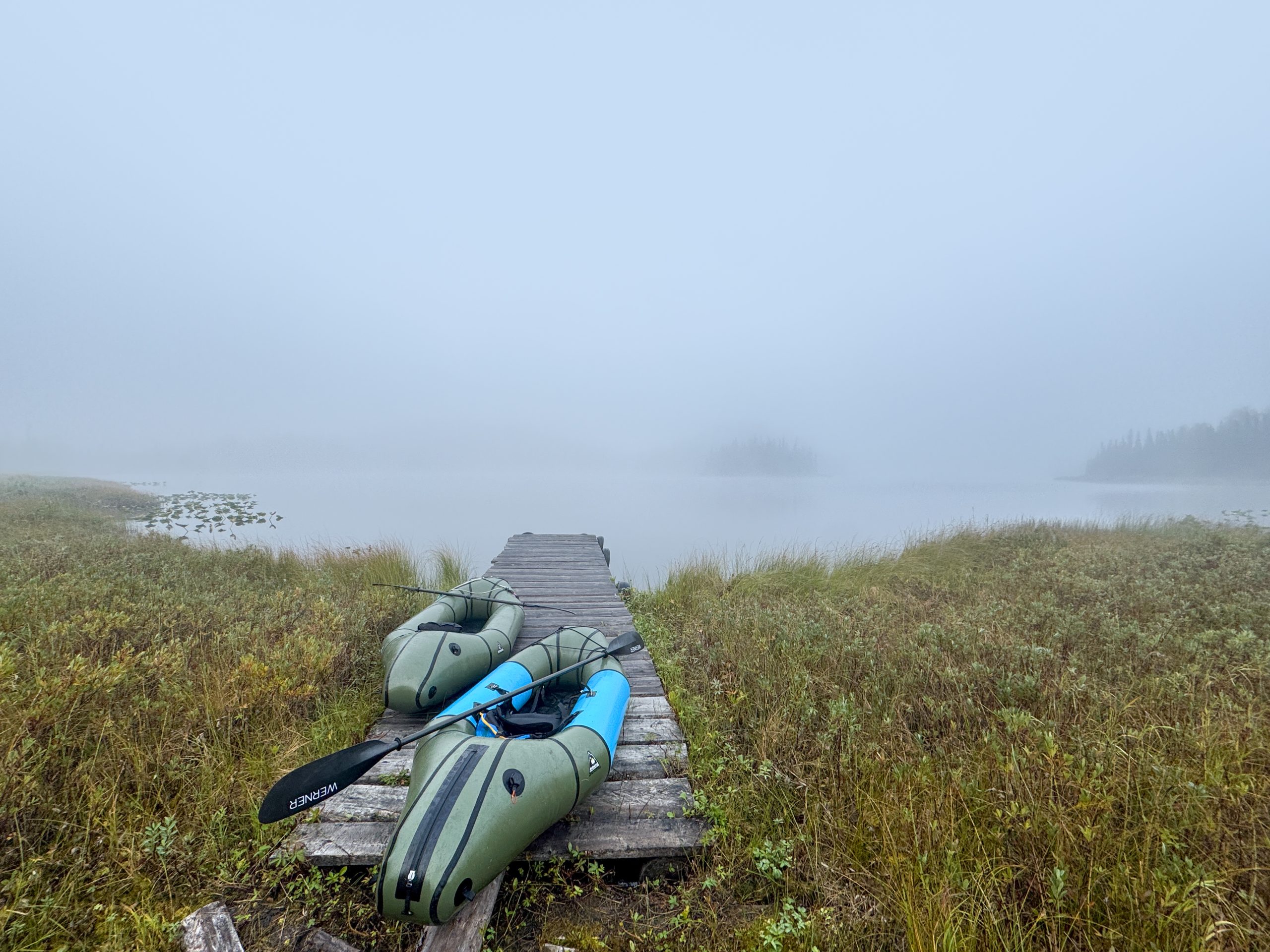 Two inflatable kayaks rest on a wooden dock by a foggy lake in Mat-Su, Alaska