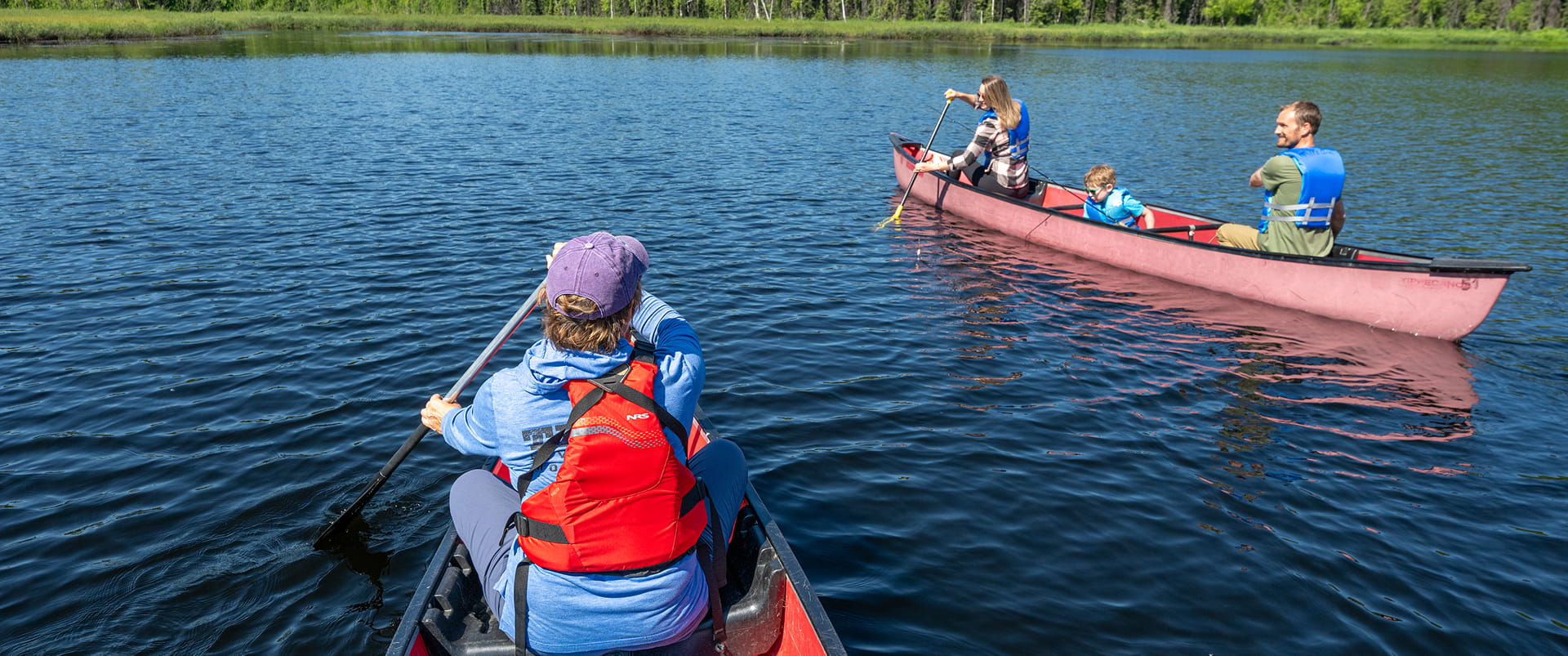 A serene lake scene with three canoes, each carrying paddlers in life jackets, enjoying a peaceful day on the water in Mat-Su, Alaska