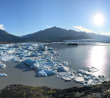 A serene glacier lagoon with floating icebergs and a backdrop of majestic mountains under a bright sun in Mat-Su, Alaska