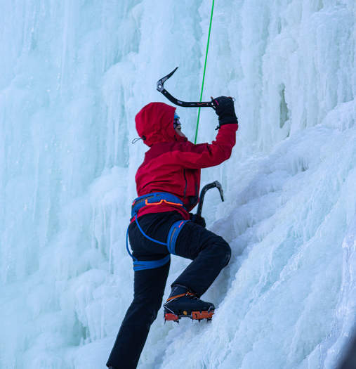 A climber in red gear ascends an icy cliff using ice axes and crampons in Mat-Su, Alaska