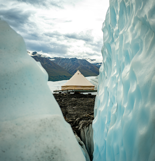 A yurt-like tent stands amidst a stunning Arctic landscape, framed by towering ice formations in Mat-Su, Alaska
