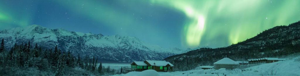 A serene winter night in a snowy mountain landscape illuminated by the mesmerizing green glow of the Aurora Borealis in Mat-Su, Alaska