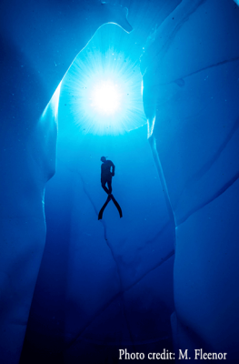 A scuba diver explores a deep blue ice cave, illuminated by a bright light source above in Mat-Su, Alaska