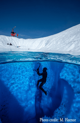 A scuba diver explores an underwater ice cave, illuminated by the light filtering through the ice above in Mat-Su, Alaska