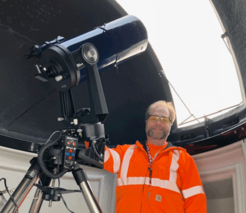 Astronomer in an orange safety vest operating a large telescope inside a domed observatory in Mat-Su, Alaska