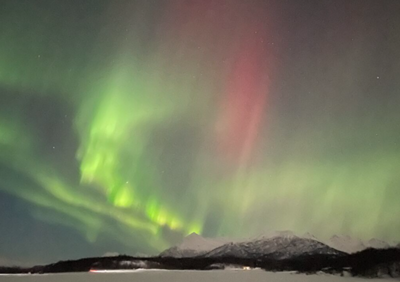 The Northern Lights dance across the night sky, painting it with vibrant hues of green and pink over a snowy mountain landscape in Mat-Su, Alaska