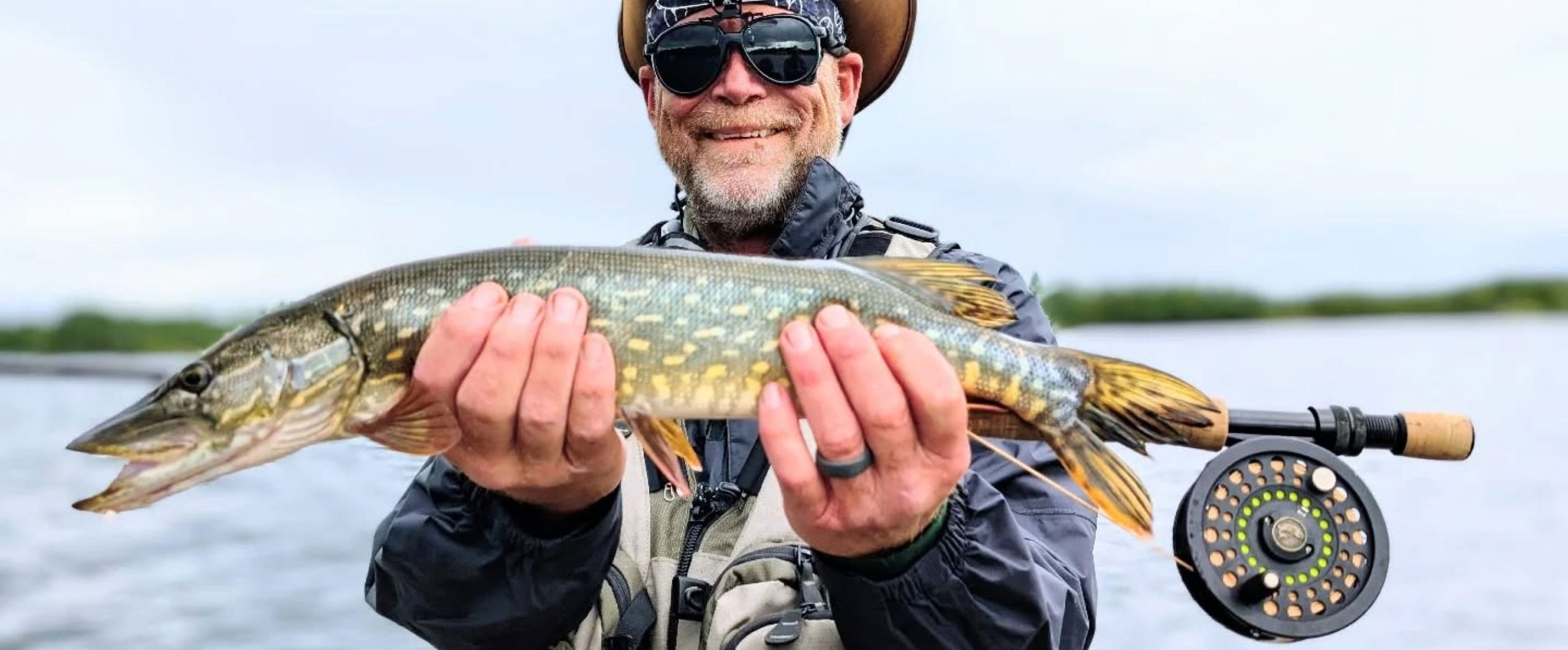 A man proudly displays a large fish he caught while fishing on a serene lake in Mat-Su, Alaska