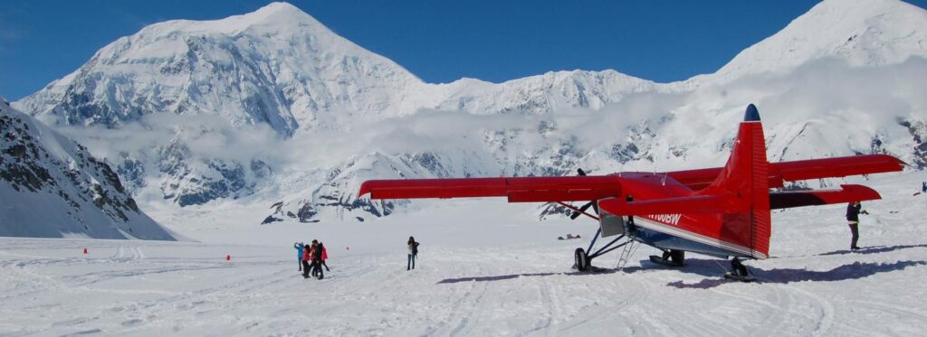A red airplane parked on a snowy glacier with a majestic mountain range in the background in Mat-Su, Alaska