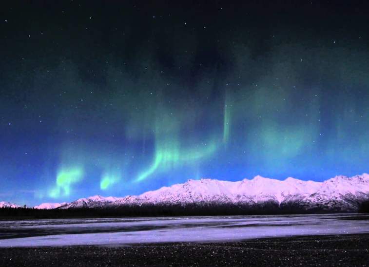 A vibrant display of the Northern Lights dances across a starry night sky above snow-capped mountains in Mat-Su, Alaska