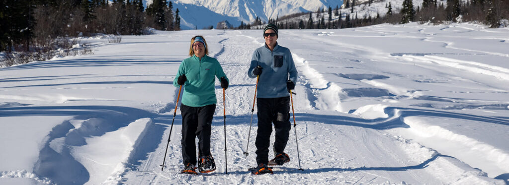 Two people snowshoeing on a snowy trail with mountains in the background in Mat-Su, Alaska