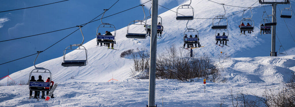 Skiers and snowboarders ride a busy ski lift up a snowy mountain slope in Mat-Su, Alaska