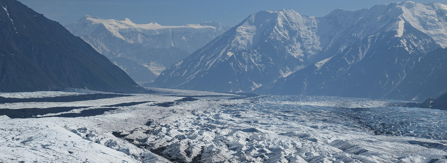A vast expanse of snow and ice stretches across a mountainous landscape, with towering peaks in the distance in Mat-Su, Alaska