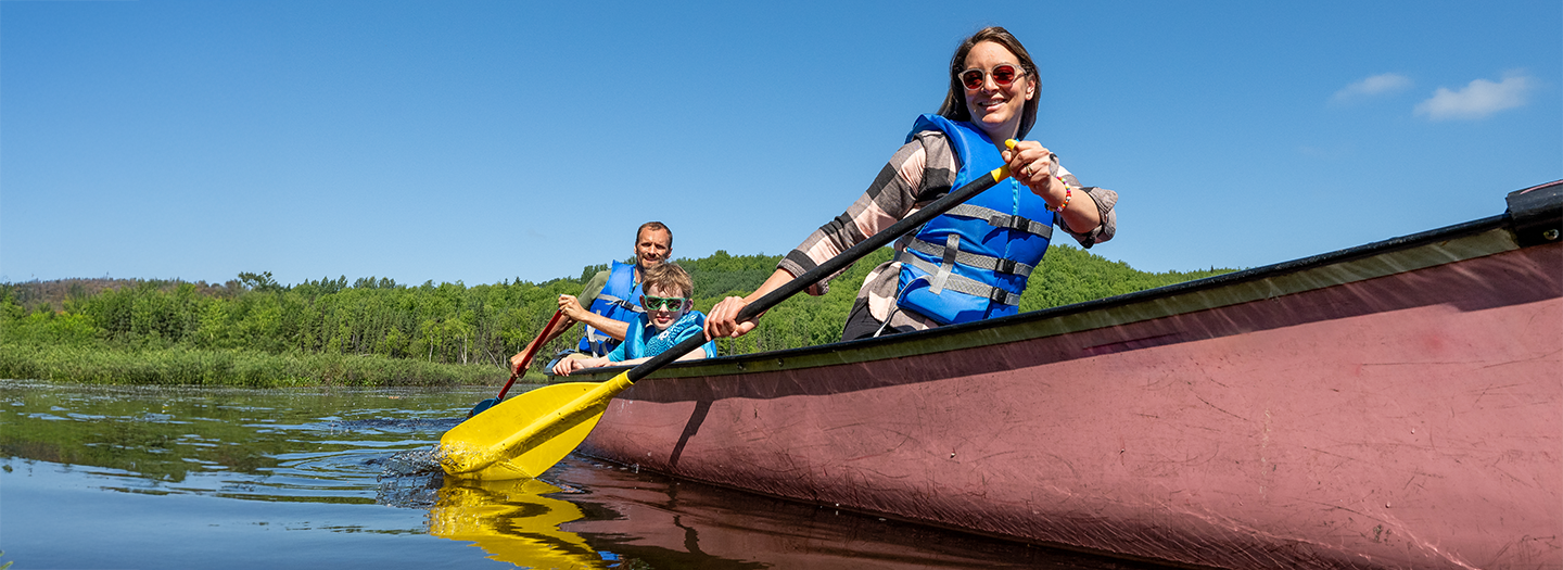 A group of people enjoying a sunny day on a calm lake, paddling a pink canoe with yellow oars in Mat-Su, Alaska