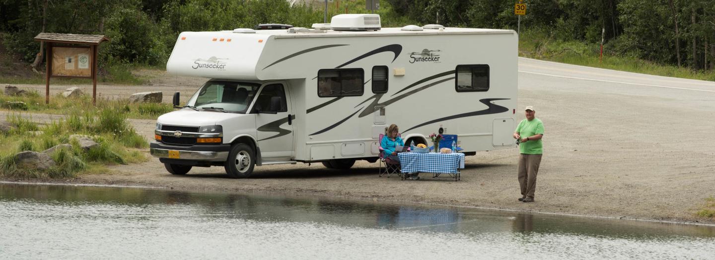 A family enjoys a peaceful lakeside camping trip in a white RV, with a serene view of the water and surrounding greenery in Mat-Su, Alaska