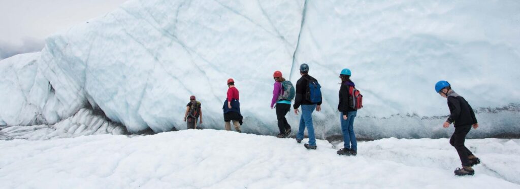 A group of adventurers in colorful gear trek across a vast glacier, surrounded by towering ice formations in Mat-Su, Alaska