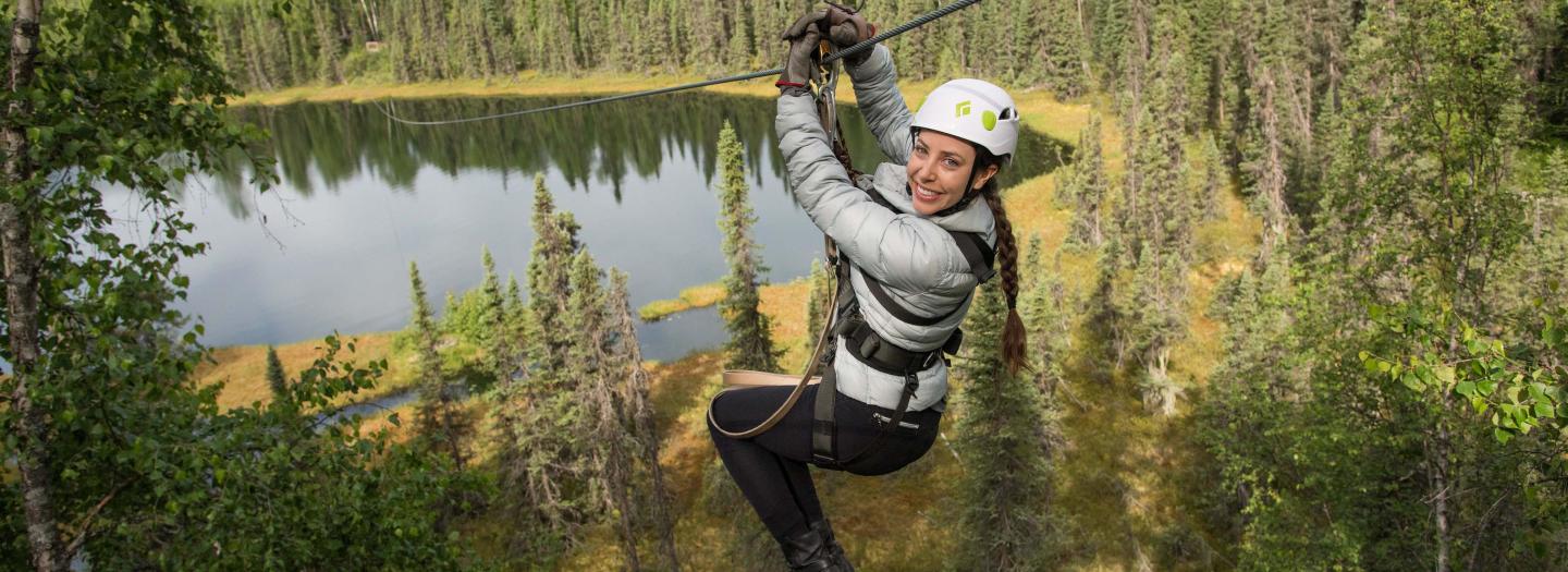 A woman zip-lining through a lush forest with a serene lake below in Mat-Su, Alaska