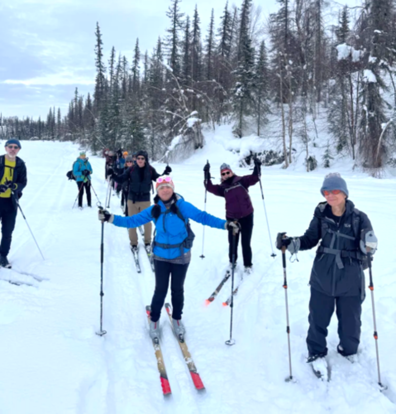 A group of skiers enjoying a sunny day on a snowy trail surrounded by trees in Mat-Su, Alaska