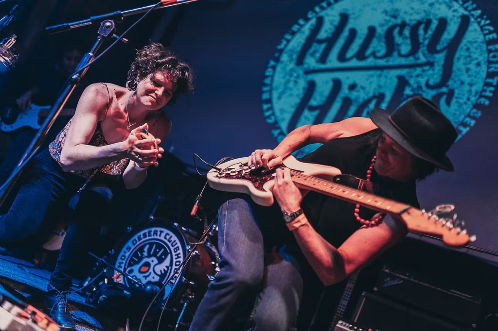 Two musicians perform on stage, one playing an electric guitar and the other singing into a microphone in Mat-Su, Alaska