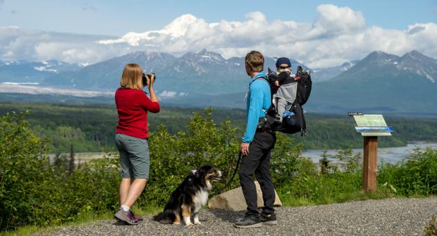 A family with a dog enjoys the view of a majestic mountain range from a scenic overlook in Mat-Su, Alaska