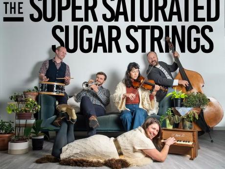 A group of five musicians play various instruments in a cozy living room filled with plants in Mat-Su, Alaska