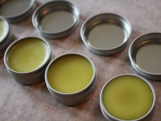 Several small metal tins filled with a bright yellow-green substance, likely a natural remedy or salve in Mat-Su, Alaska