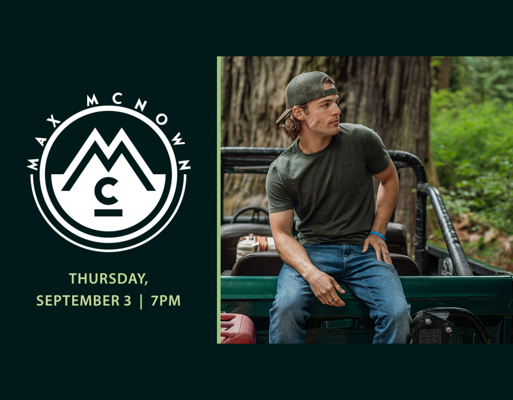 A man wearing a green t-shirt and jeans sits on the back of a green truck in a forest setting in Mat-Su, Alaska