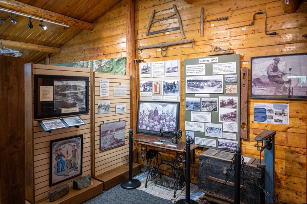 A rustic wooden cabin interior filled with historical exhibits, including framed photographs, documents, and vintage tools in Mat-Su, Alaska