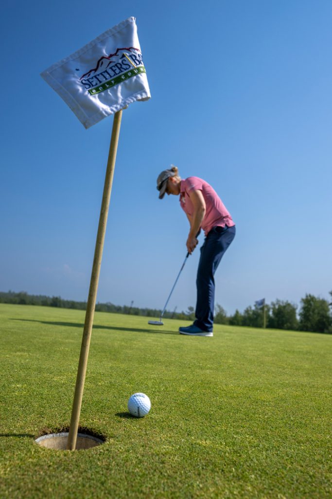 A golfer in a pink shirt and cap lines up a putt on a sunny day at Settlers Bay Golf Course in Mat-Su, Alaska
