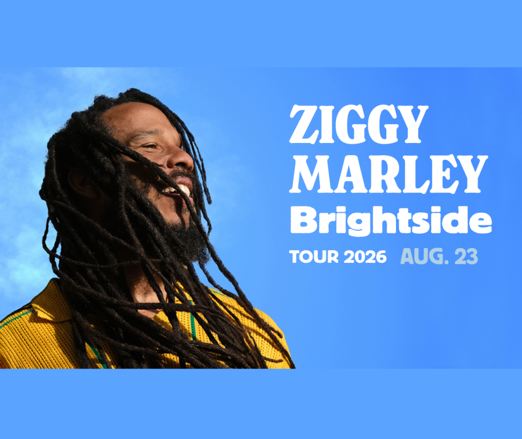 Ziggy Marley performs with a joyful expression against a bright blue sky in Mat-Su, Alaska