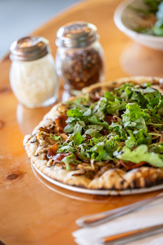 A gourmet pizza topped with arugula and balsamic glaze on a wooden table in Mat-Su, Alaska