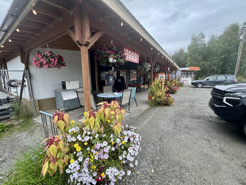 A rustic building with a covered porch featuring outdoor seating and hanging flower baskets in Mat-Su, Alaska