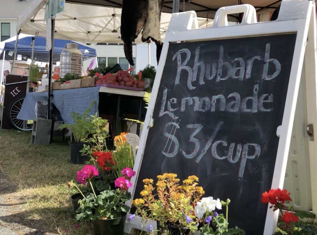 A chalkboard sign advertising rhubarb lemonade for three dollars a cup at a market in Mat-Su, Alaska