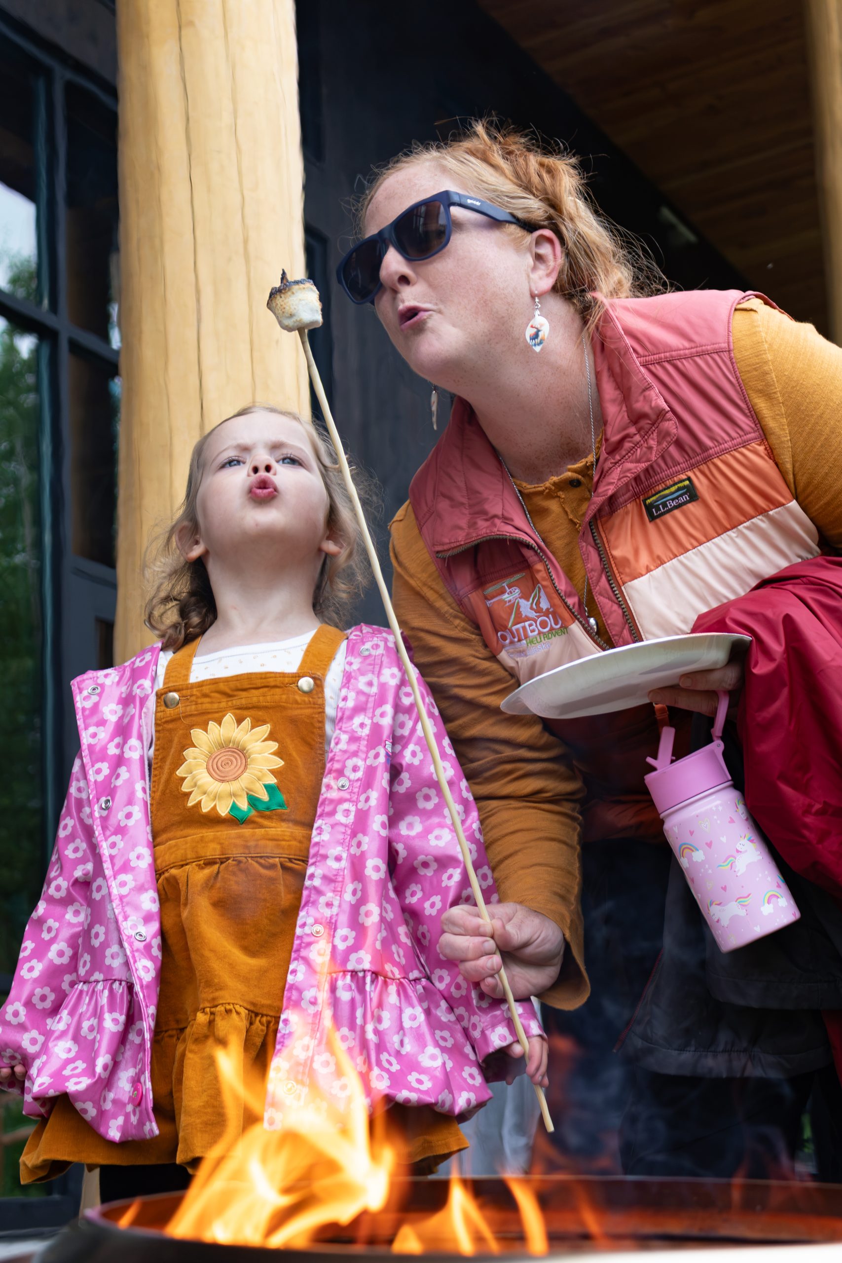 A woman and a young girl blowing on a roasted marshmallow over a fire in Mat-Su, Alaska