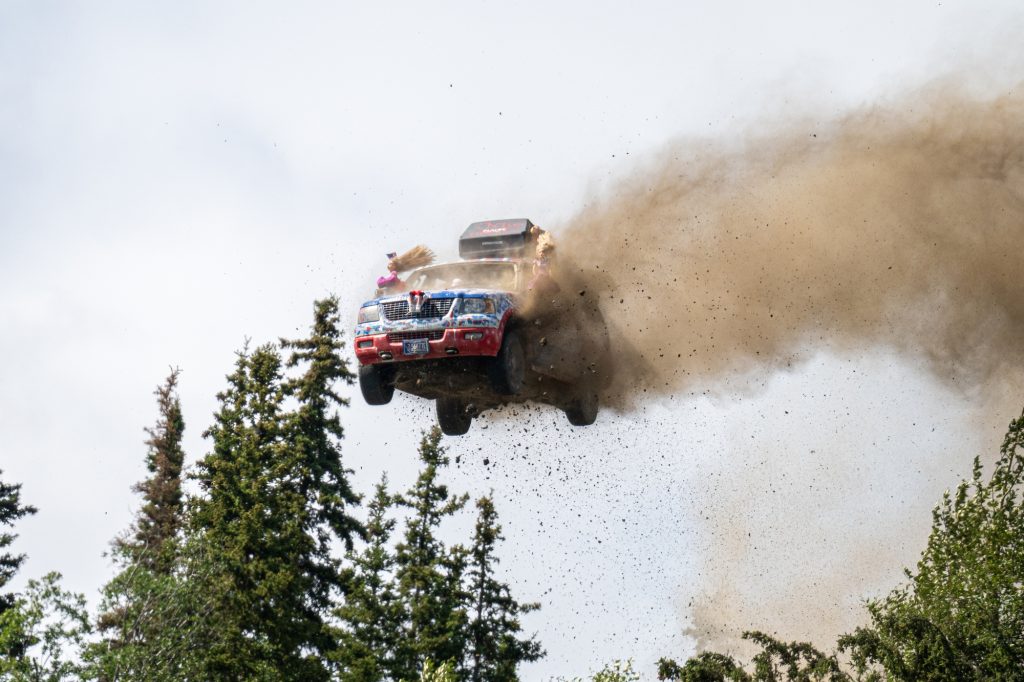 A rally truck jumps high into the air, kicking up a large cloud of dust in Mat-Su, Alaska